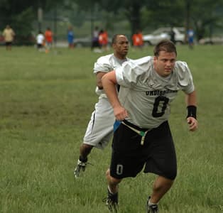 A big lineman firing off the line ahead of a teammate in a flag football game