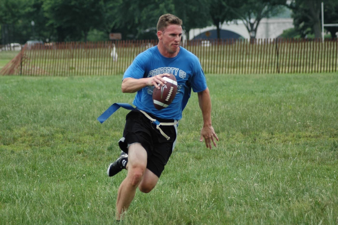 Quarterback in a blue shirt scrambling out of the pocket with the ball in a flag football game
