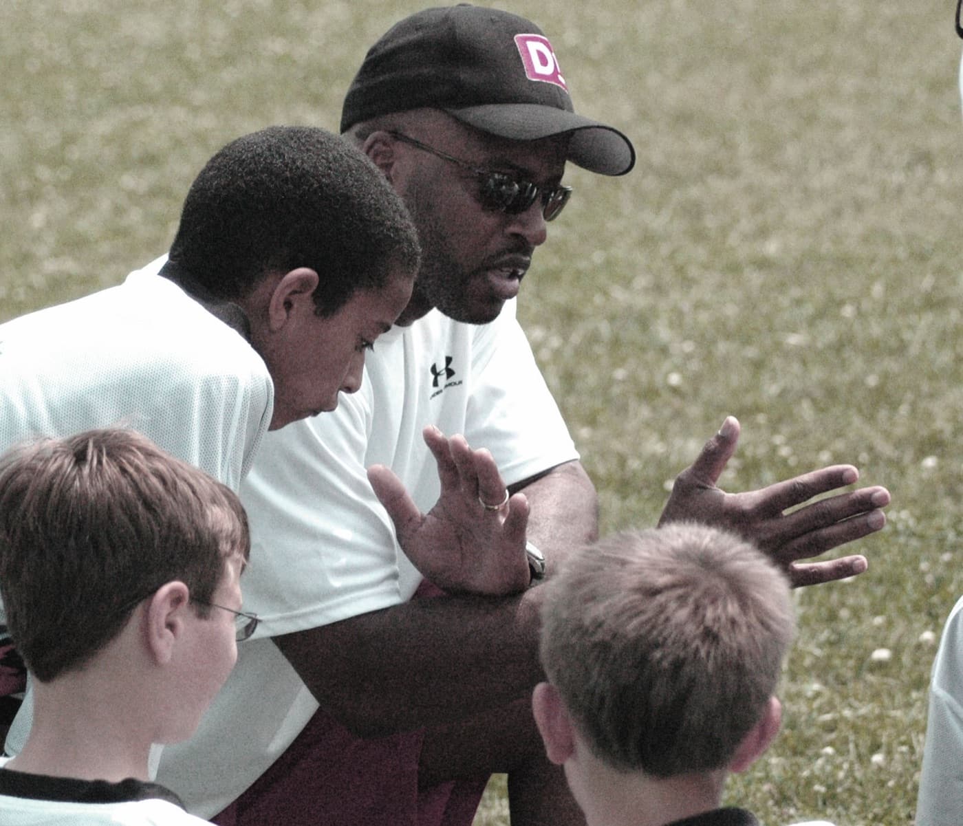 A coach kneeling with young players, talking them through a play